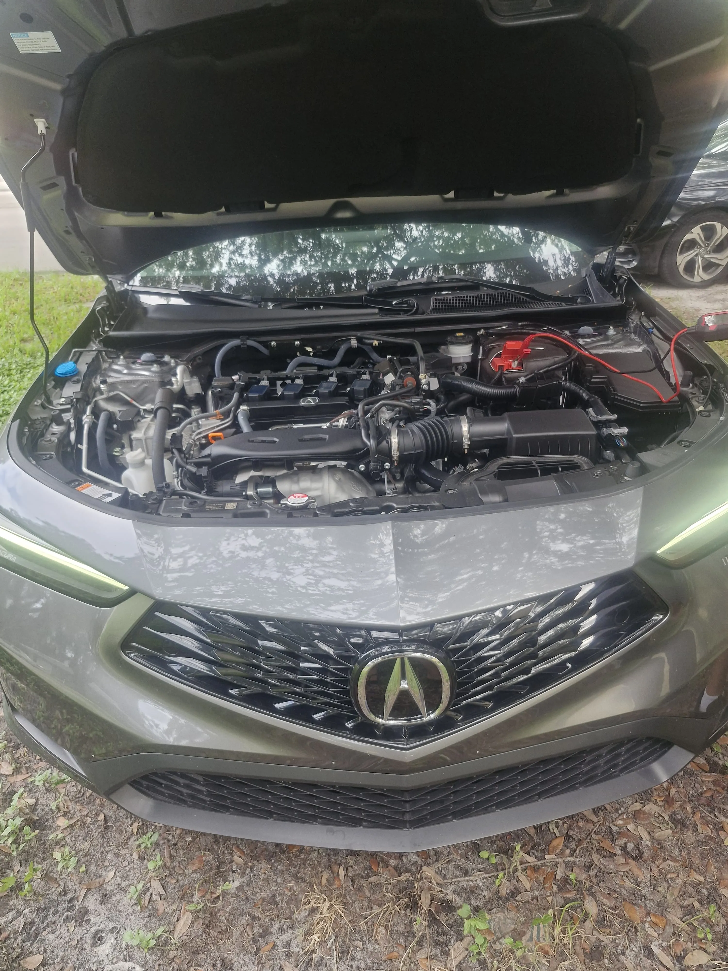 Acura con el capó abierto y equipo de asistencia para batería conectado