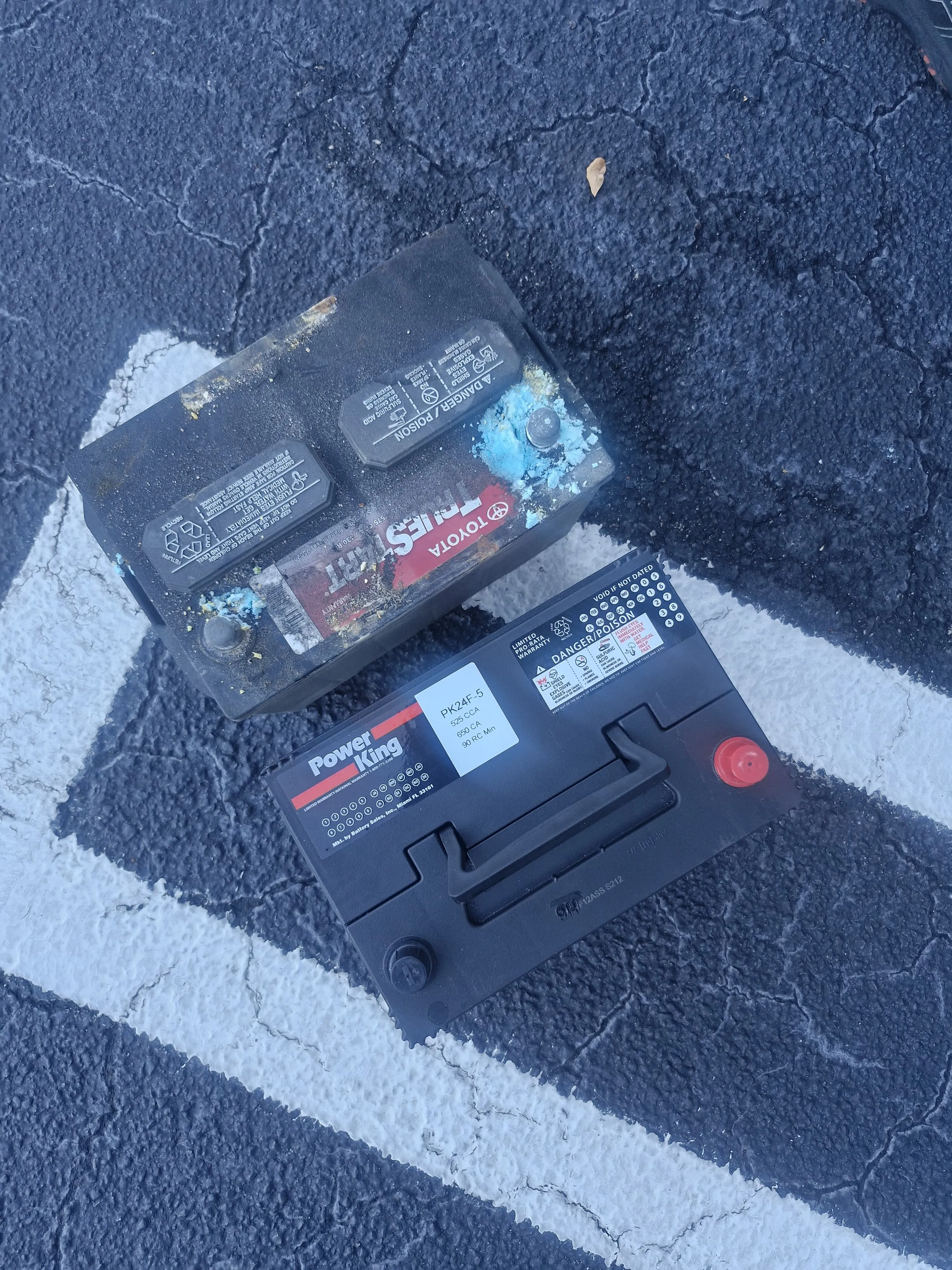 Batería Toyota con corrosión junto a una batería Power King limpia sobre el pavimento